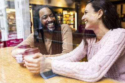 Happy multiracial couple sitting with coffee cups in cafe
