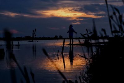 Silhouette man standing by sea against sky during sunset