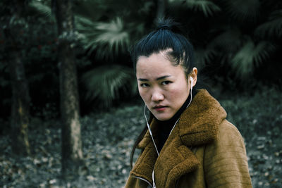 Portrait of woman listening music against trees