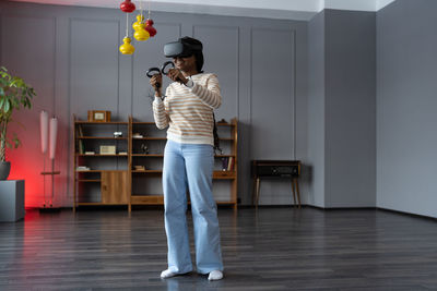 Happy young african american woman wearing virtual reality goggles playing video games at home