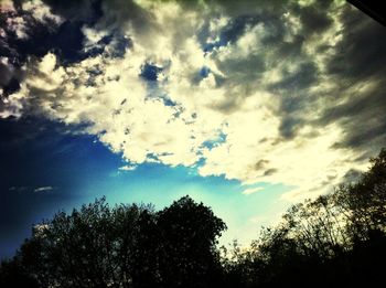 Low angle view of trees against cloudy sky