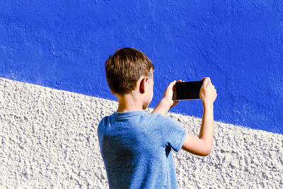 Boy photographing against blue wall