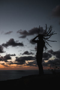 Silhouette person with dreadlocks standing on land against sky during sunset 