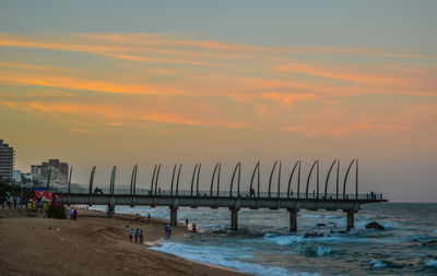 Wooden posts on beach against sky during sunset