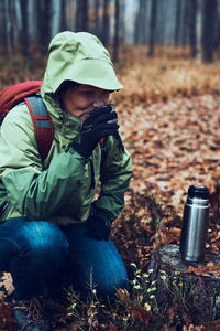 Woman with backpack having break during autumn trip drinking a hot drink from thermos flask