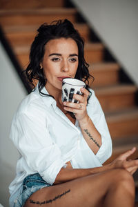 Beautiful woman drinking coffee sitting on staircase at home