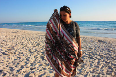 Girl at sea sunset on beach front of water with towel in hand looks ashore in rosignano tuscany