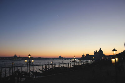 Silhouette buildings by sea against clear sky during sunset