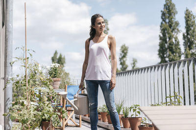 Smiling woman on balcony holding watering can