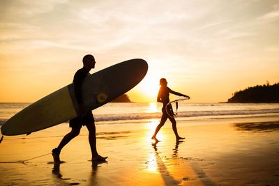 Silhouette men on beach against sky during sunset