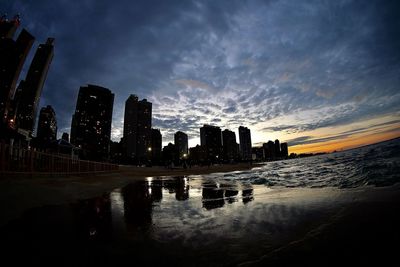 Silhouette buildings by city against sky at sunset