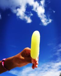 Close-up of hand holding ice cream against blue sky