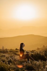 Man sitting on land against sky during sunset