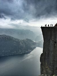 Silhouette people standing at preikestolen by river against cloudy sky