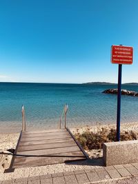 Information sign by sea against clear blue sky