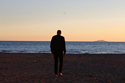 Rear view of man walking on beach against clear sky