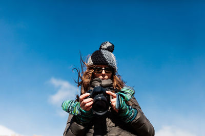 Low angle view of man photographing against blue sky