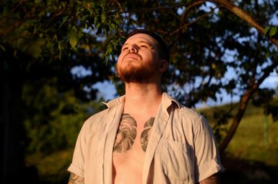 Young man looking away against trees