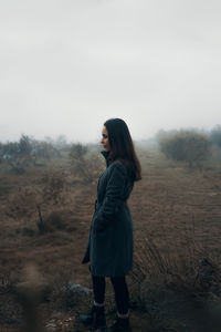 Side view of woman standing on field against foggy sky