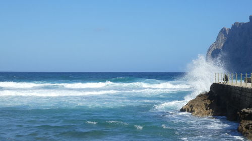 Waves splashing on rocky shore  against clear sky