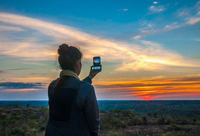 Rear view of man photographing against sky during sunset