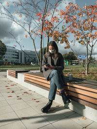 Woman sitting on bench against footpath