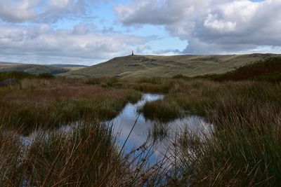 Scenic view of moorland with stoodley pike in the distance and pond in the foreground