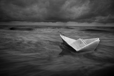 Paper boat floating on sea against sky