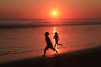 Silhouette men on beach against sky during sunset