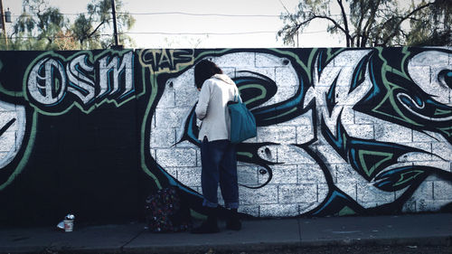 Rear view of man standing against graffiti wall