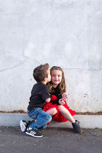 Full length of mother and girl wearing hat against wall