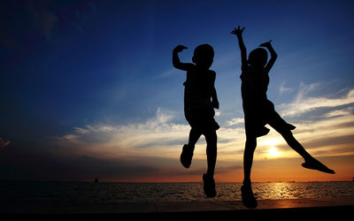 Silhouette man jumping on sea against sky during sunset