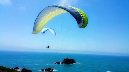 Mid adult man paragliding over sea against blue sky during sunny day