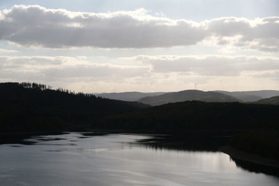 Scenic view of lake by silhouette mountain against sky