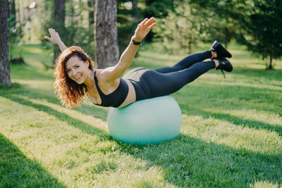 Portrait of woman with arms outstretched exercising on fitness ball in park