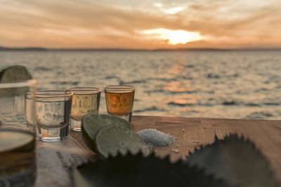 Tequila in shot glasses on table against sea during sunset