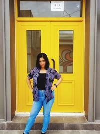 Portrait of young woman standing against yellow door of building