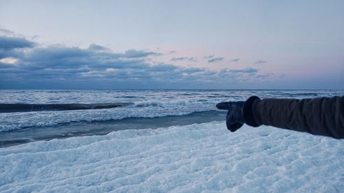 Close-up of person pointing at frozen sea against sky during sunset