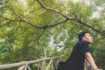 Side view of young man looking away against trees