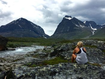 Rear view of woman sitting on rock against mountains during winter