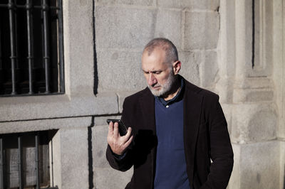 Adult man in suit looking at mobile phone against wall