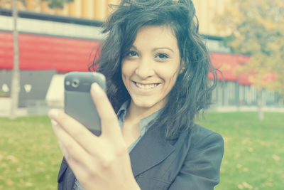 Portrait of a smiling young woman using mobile phone in city