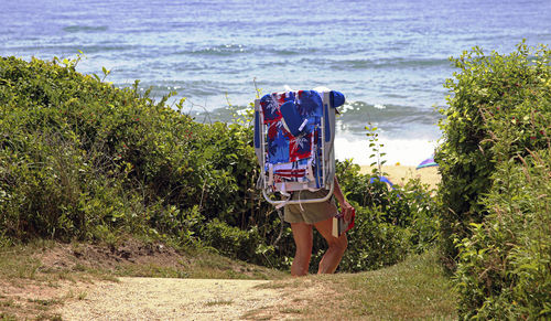 A women heading to the beach in montauk walking through the dunes carrying a book and beach chair.