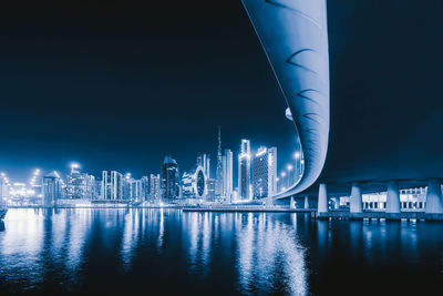 Illuminated buildings by river against sky at night