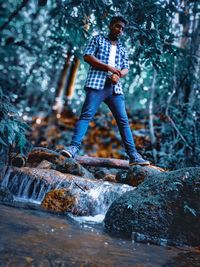 Full length of young man standing on rock in forest