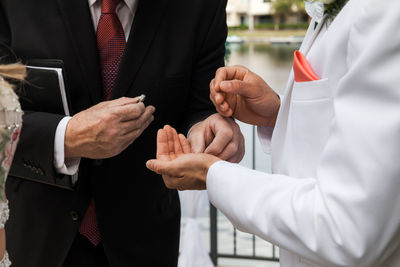 Midsection of priest giving wedding ring to groom during wedding ceremony