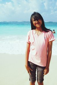 Smiling woman standing on sand at beach against cloudy sky