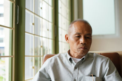 Mature man sitting on chair by window at home