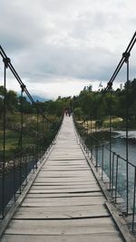 Walkway leading to pier against cloudy sky