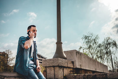 Young man using smart phone against sky